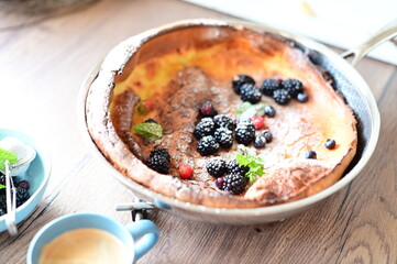 Beautiful close-up of a Dutch Baby pancake breakfast dessert topped with fresh fruit and a dusting of powdered sugar. The golden, fluffy pancake combined with vibrant berries