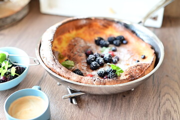 Traditional Dutch baby pancake served for breakfast, a popular European dish. The fluffy baked pancake is topped with fresh fruit, powdered sugar, and mint leaves, beautifully styled on a light.