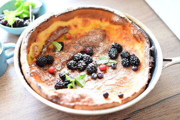 Beautiful close-up of a Dutch Baby pancake breakfast dessert topped with fresh fruit and a dusting of powdered sugar. The golden, fluffy pancake combined with vibrant berries