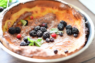 Beautiful close-up of a Dutch Baby pancake breakfast dessert topped with fresh fruit and a dusting of powdered sugar. The golden, fluffy pancake combined with vibrant berries