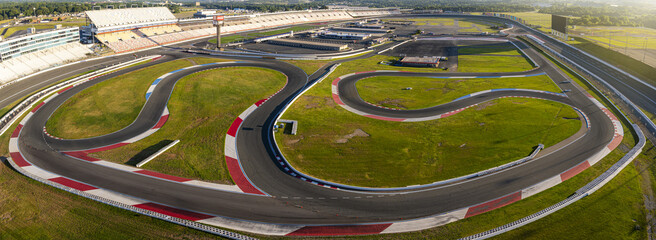 Concord, United States - 28 July 2025: Aerial view of a race track's winding asphalt curves cutting through vibrant green fields, contrasted by the stark white and red safety barriers.