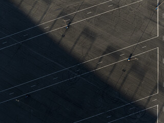 Concord, United States - 28 July 2025: Aerial view of a stark parking lot, shadows stretch diagonally across the asphalt, creating a dramatic contrast with the bright white lines.