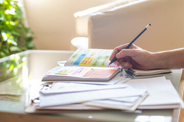 Person writing notes on a paper notebook, organizing work or personal agenda at home, using sticky notes, pencil and paper documents, planning future appointments and meetings
