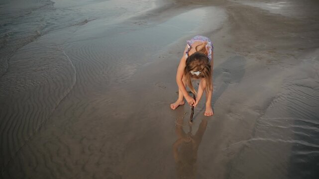 Child's hand drawing heart on sand at the beach during sunset in a serene coastal setting