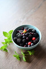 Blue bowl filled with fresh summer fruits, including ripe blueberries and blackberries, set against a clean white background.