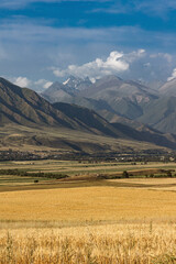 Kyrgyzstan autumn landscape. Village, agricultural fields and high mountains. Rural scene