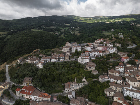 Aerial view of sun-drenched rooftops and winding streets nestled amidst rolling hills and verdant forests, Morcone, Benevento, Campania, Italy.