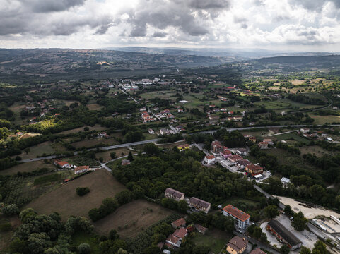 Aerial view of the patchwork landscape where terracotta roofs nestle among emerald trees under a sky streaked with silver and grey, Morcone, Benevento, Campania, Italy.
