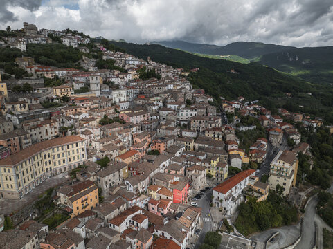 Aerial view of terracotta rooftops cascading down the hillside, nestled among verdant trees under a dramatic sky, Morcone, Benevento, Campania, Italy.