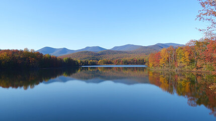 Fototapeta premium Stunning autumn reflections mirror vibrant forest colors across tranquil waters. Mountain peaks rise under a clear blue sky.