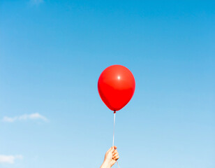 Hand holding red balloon on blue sky