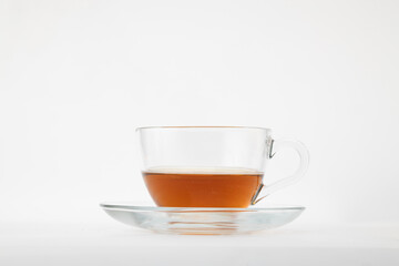 A clear glass teacup filled with amber-colored tea, possibly black or rooibos, resting on a matching clear glass saucer