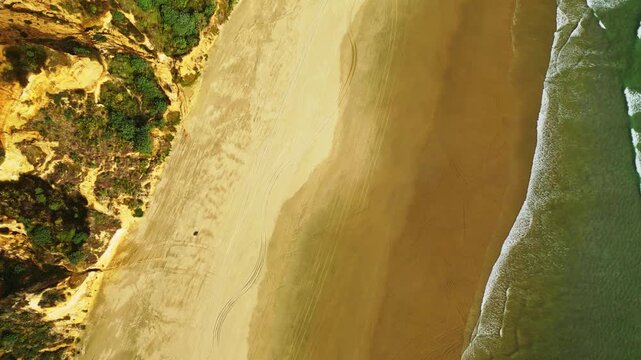 Aerial view of waves crashing onto a sandy beach, contrasting with the lush green vegetation on the adjacent cliffs, Dargaville, Northland Region, New Zealand.