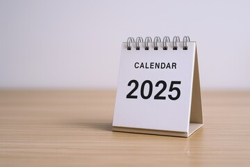 Desktop Calendar Displaying 2025 Year on Wooden Desk Against White Background, Symbolizing Future Planning and Organization