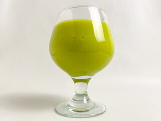 green-colored avocado smoothie in a wine glass on a white table