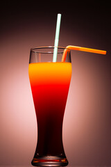 A vibrant cocktail in a tall glass, featuring distinct layers of orange, red, and dark red brown, with two straws 