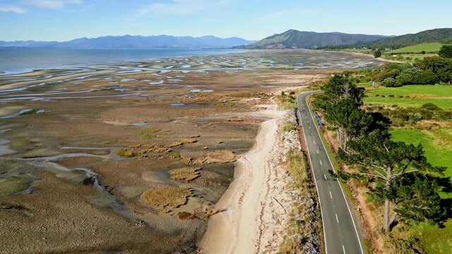 Aerial view of Wharariki Road winding along the sandy coastline, contrasting with the blue sea and green fields, Puponga, New Zealand.