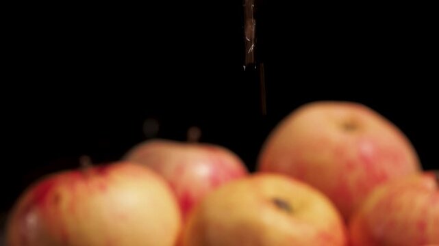 Close-up of drops falling from a ripe red apple into a glass of apple cider vinegar. The camera slowly pans down, following the drops in a smooth cinematic motion.