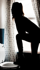 A person silhouetted in a bathroom, standing near a window.