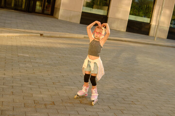 Joyful young girl with pink glasses skating outdoors at sunset, wearing casual black top, denim shorts with shirt tied around waist, capturing carefree childhood fun and energetic city lifestyle
