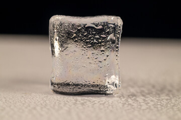 A single, clear ice cube, prominently displayed against a blurred background that transitions from 