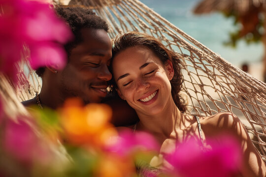 Happy multicultural couple relaxing together in a hammock surrounded by vibrant tropical flowers on a sunny beach