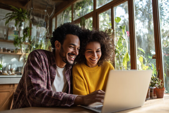 Happy young couple enjoying time together while using laptop in cozy sunlit home surrounded by plants