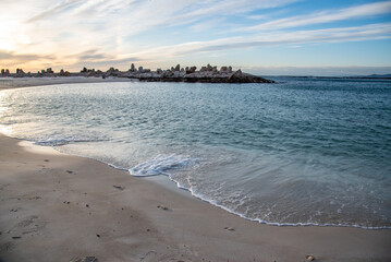 Scenic coastal view with calm sea, sandy beach, and rock formations under a vibrant sky at sunset