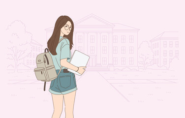 female student holding laptop standing in front of university building