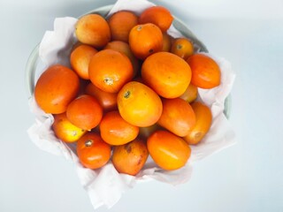 A vibrant overhead shot of a bowl filled with ripe, orange tomatoes resting on white paper. Perfect for illustrating healthy eating, fresh produce, and culinary themes.