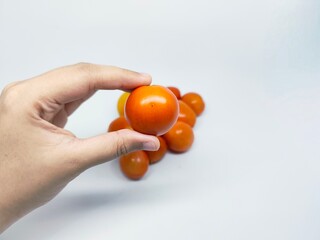 Close-up shot of a hand holding a single ripe orange cherry tomato with a group of tomatoes in the...