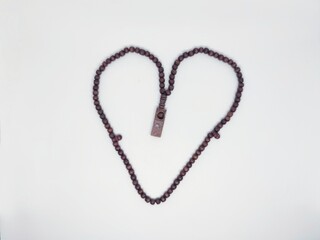 A heart-shaped rosary made of dark beads lies against a clean white background. This image symbolizes faith, love, and spirituality, perfect for religious or inspirational content.