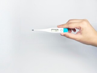 Obraz premium A hand holding a digital thermometer against a clean white background, indicating a temperature reading. The image focuses on healthcare and medical diagnostics.