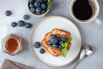 Stack of pancakes with blueberries, honey and cup of coffee on grey concrete background, table top view