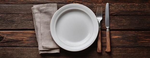 Empty white plate, fork, and knife on a rustic wooden table with a linen napkin