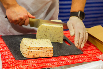Hands slicing cheese on a black cutting board with colorful textile underneath for culinary...