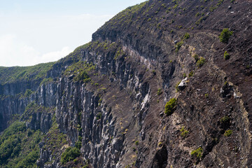 Rugged volcanic cliff face with sparse green vegetation and dramatic rocky terrain under a clear sky, natural landscape