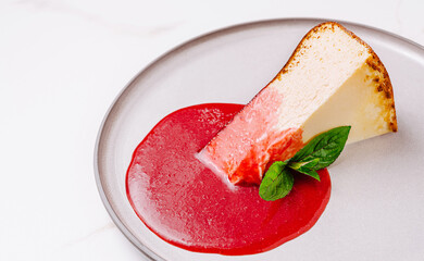 Delicious slice of cheesecake with raspberry sauce and mint garnish on a plate