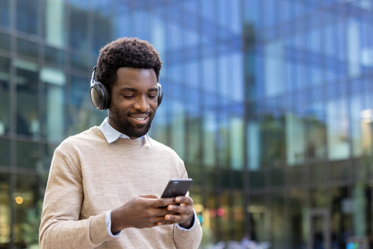 A cheerful individual enjoying music on headphones interacting on their smartphone in an urban setting. Demonstrates the modern lifestyle combining technology and enjoyment in a relaxed environment.
