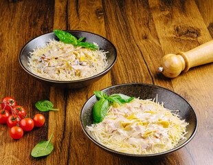 Delicious pasta served in bowls with cherry tomatoes and basil on wooden table