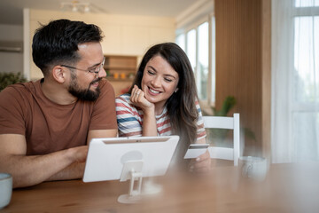 Happy couple making online payment using tablet and credit card at home