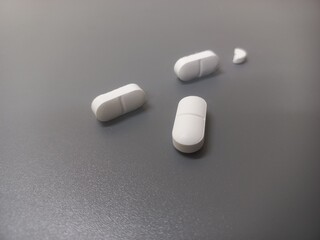 Four white oblong tablets, one of which is broken into two pieces,are placed on a smooth gray surface. Each tablet has a rounded line in the middle,making it easy to break for accurate dosing or sama