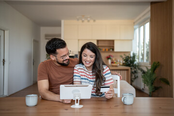 Happy couple making online payment using tablet and credit card at home