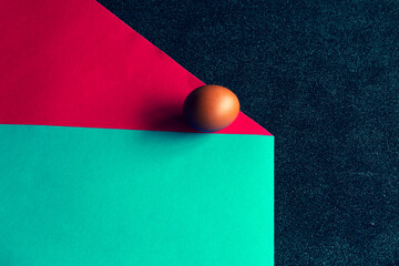 Minimalist composition with brown egg on red and teal background