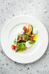 Elegant vegetarian appetizer with grilled eggplant, cherry tomatoes, herbs, and creamy sauce, artistically plated on a white dish over a gray textured background