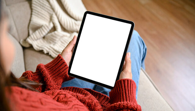 Close-up of woman’s hand holding tablet with white screen and Christmas background, ideal for holiday content and tech promotions