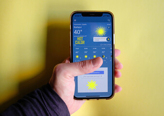 Mano con móvil y aplicación de tiempo soleado y temperaturas altas con sol y calor de cuarenta...