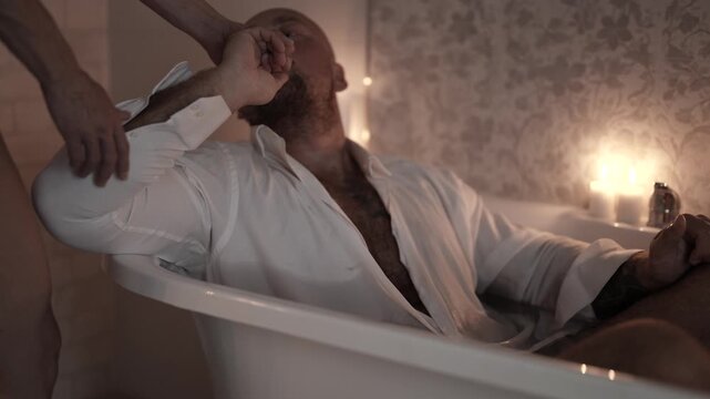 A man kisses a woman's hand, she stands next to him, the frame is full of tenderness and hidden passion.