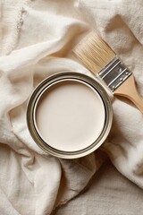 Overhead view of an open white paint can and paintbrush on a neutral drop cloth. Home renovation and DIY project concept.