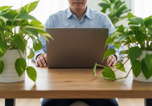 Man working on laptop surrounded by lush green plants in a bright modern office setting - Powered by Adobe